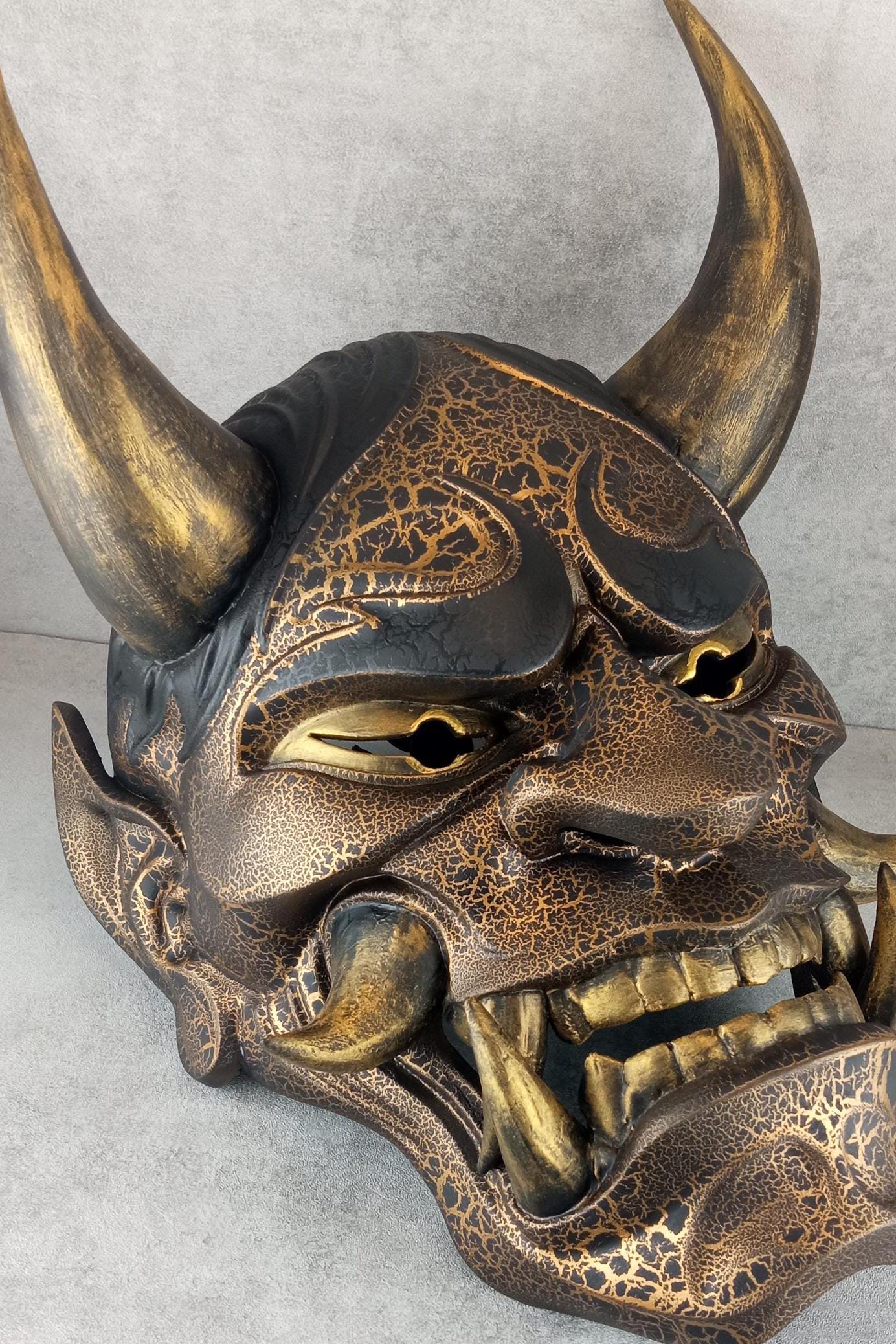 Schwarze und goldene rissige traditionelle Hannya-Maske mit großen schwarzen Augenbrauen
