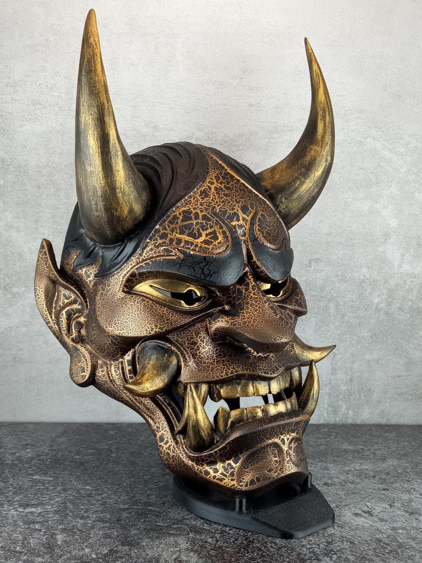 Schwarze und goldene rissige traditionelle Hannya-Maske mit großen schwarzen Augenbrauen