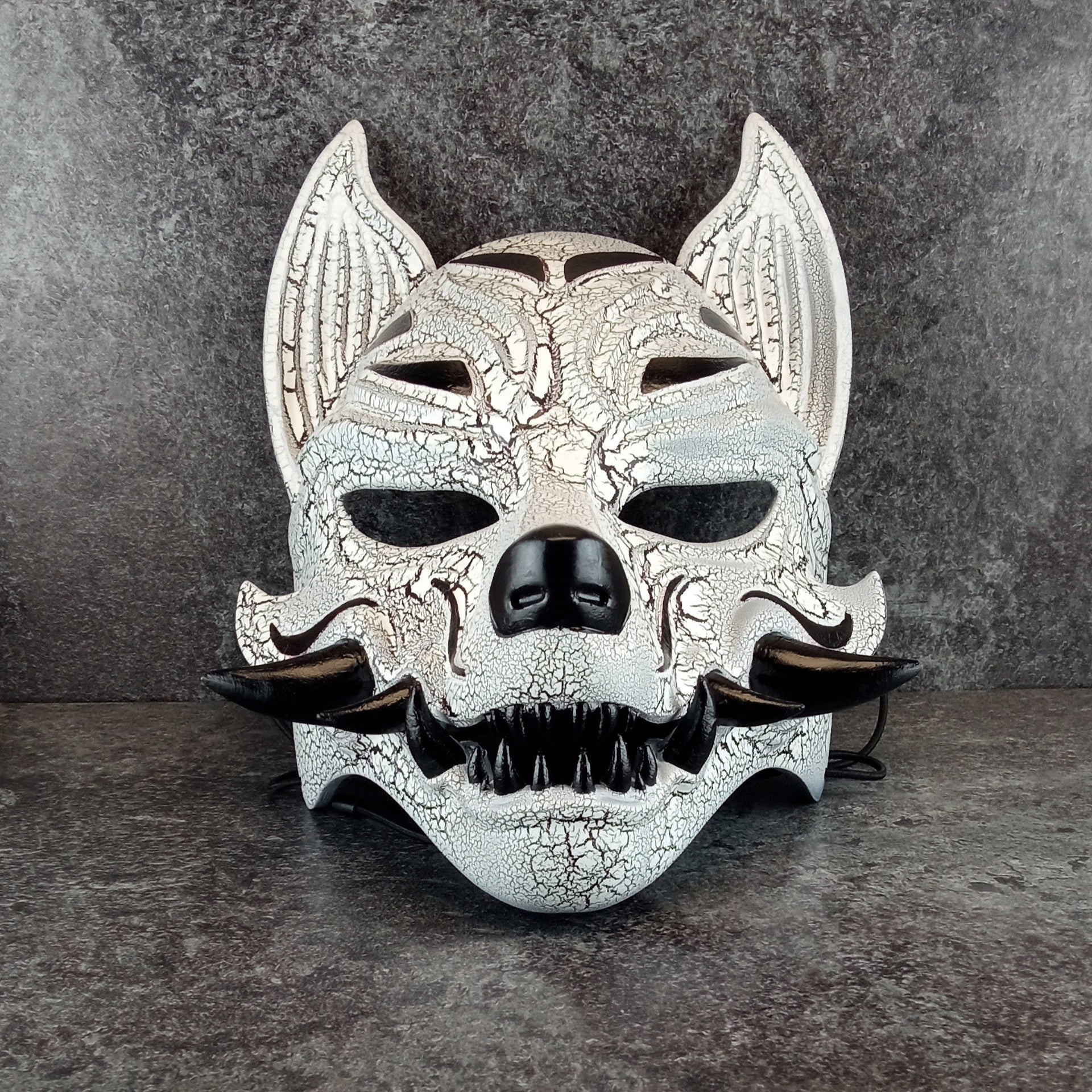 Schwarz-weiße rissige Kitsune (Okami)-Maske mit schwarzen Reißzähnen