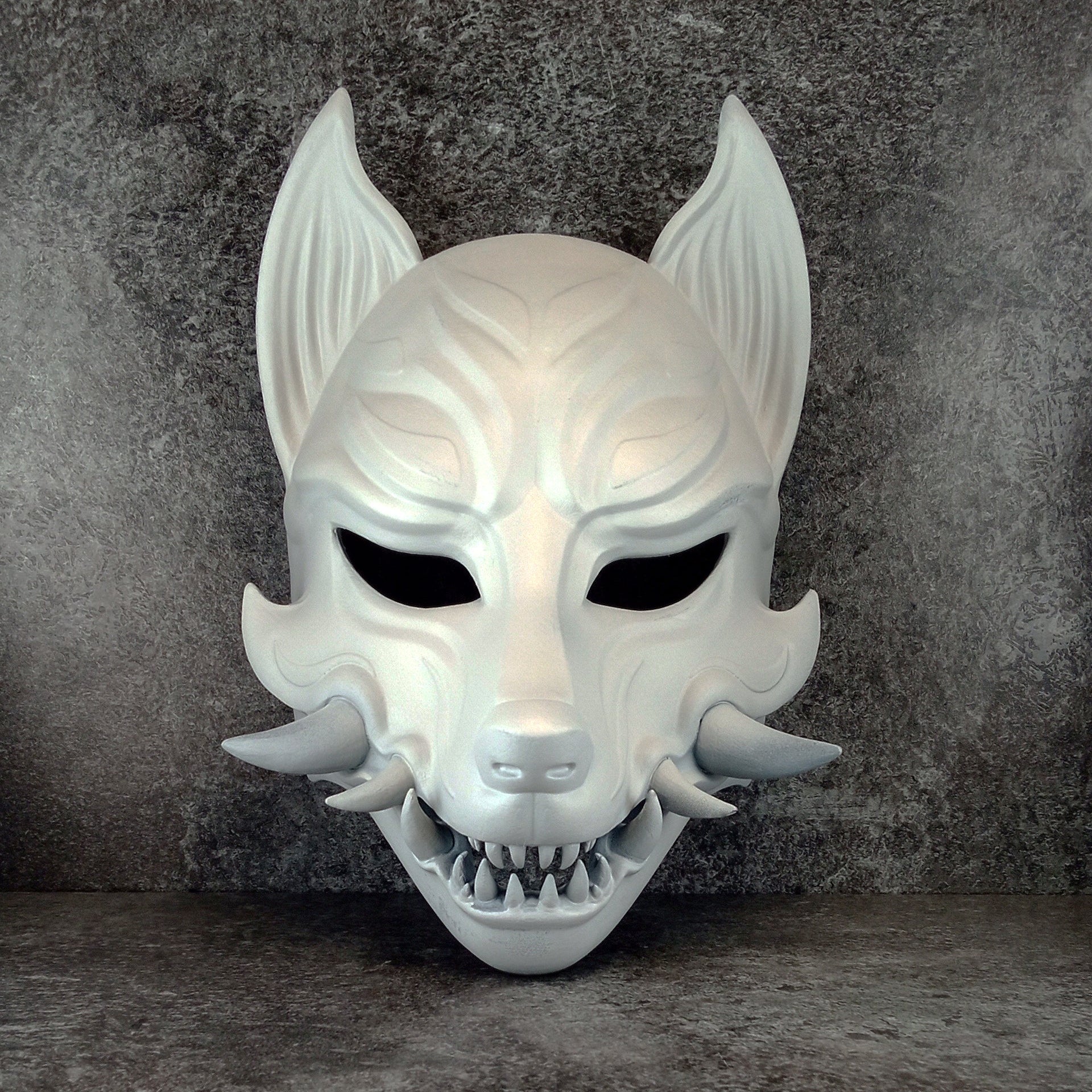 Schwarz-weiße rissige Kitsune (Okami)-Maske mit schwarzen Reißzähnen