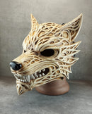 A 3D-printed wolf mask with intricate cutout patterns, displayed on a brown mannequin head against a gray concrete-textured background.
