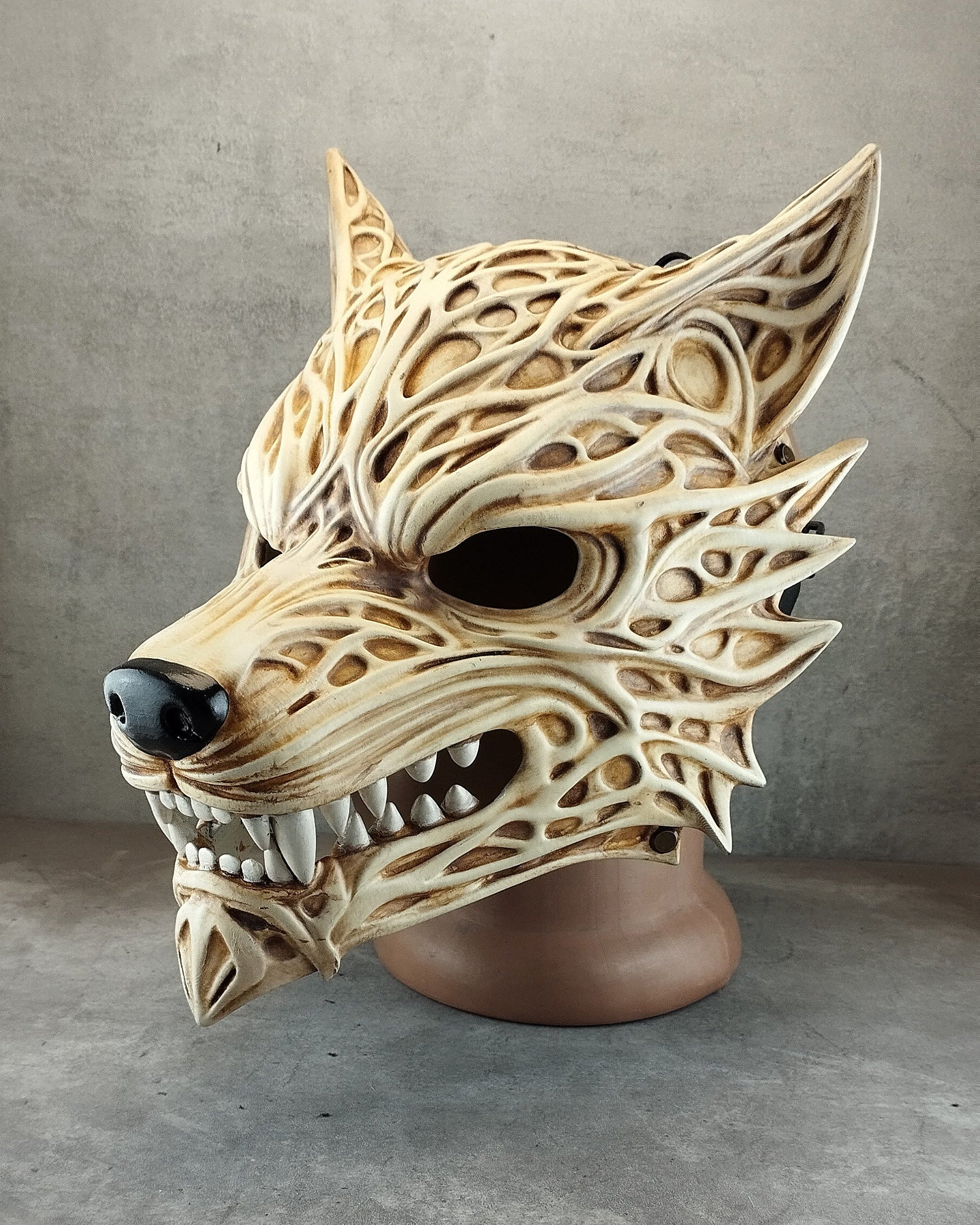 A 3D-printed wolf mask with intricate cutout patterns, displayed on a brown mannequin head against a gray concrete-textured background.