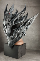 A highly detailed, metallic silver and black fantasy helmet with sharp flame-like spikes and intricate carvings, displayed on a black pedestal against a textured gray studio background.