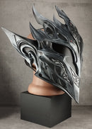A large, ornate fantasy-style helmet with sharp angular spikes and dark metallic detailing, displayed on a mannequin head mounted atop a black pedestal against a textured gray wall.