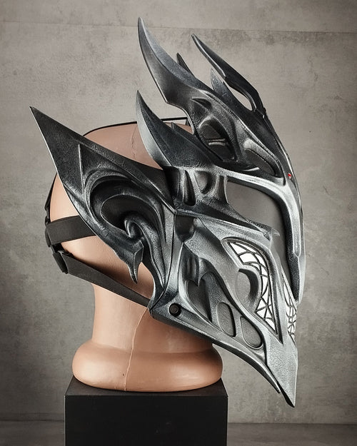 A black and silver fantasy warrior helmet displayed on a mannequin head mounted on a black pedestal against a gray concrete wall.