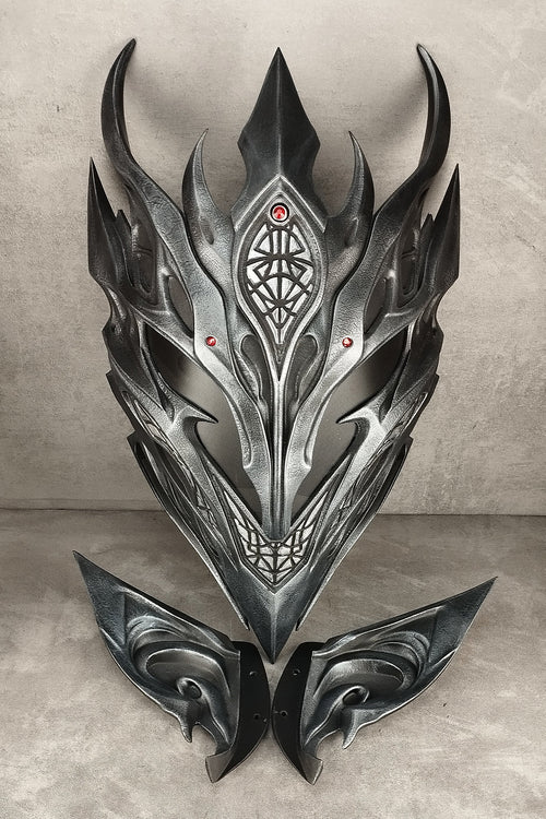 A dark metallic fantasy mask with sharp angular horns and symmetrical wing-like side pieces, displayed against a textured gray backdrop.