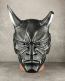 A black and silver horned demon mask displayed on a mannequin head against a gray concrete wall and floor.