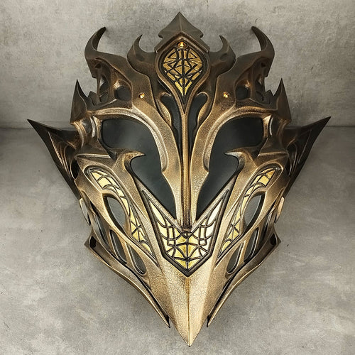 A fantasy-style metallic elf mask with ornate gold and black detailing, photographed against a gray concrete wall and floor.