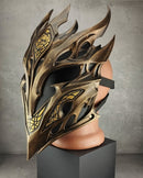 A metallic fantasy-style elf mask with sharp angular spikes and gold decorative linework, displayed on a flesh-toned mannequin head mounted over a black pedestal in a gray studio setting.