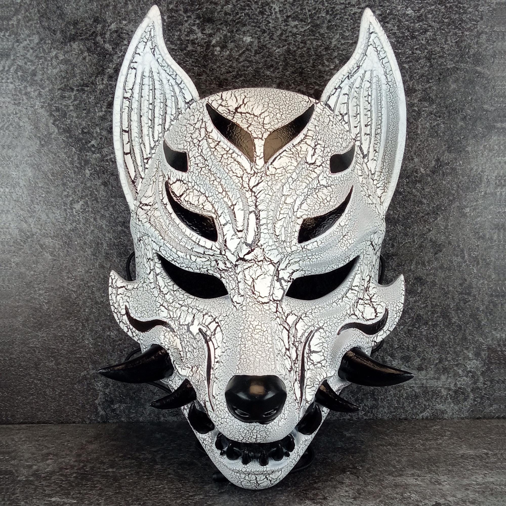 Schwarz-weiße rissige Kitsune (Okami)-Maske mit schwarzen Reißzähnen